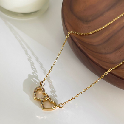 Gold necklace with heart-shaped links on a white surface with a wooden block in the background