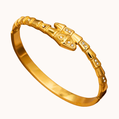 A polished yellow gold hinged bangle bracelet with a snake-head clasp adorned with small clear stones, shown on a plain off-white background.