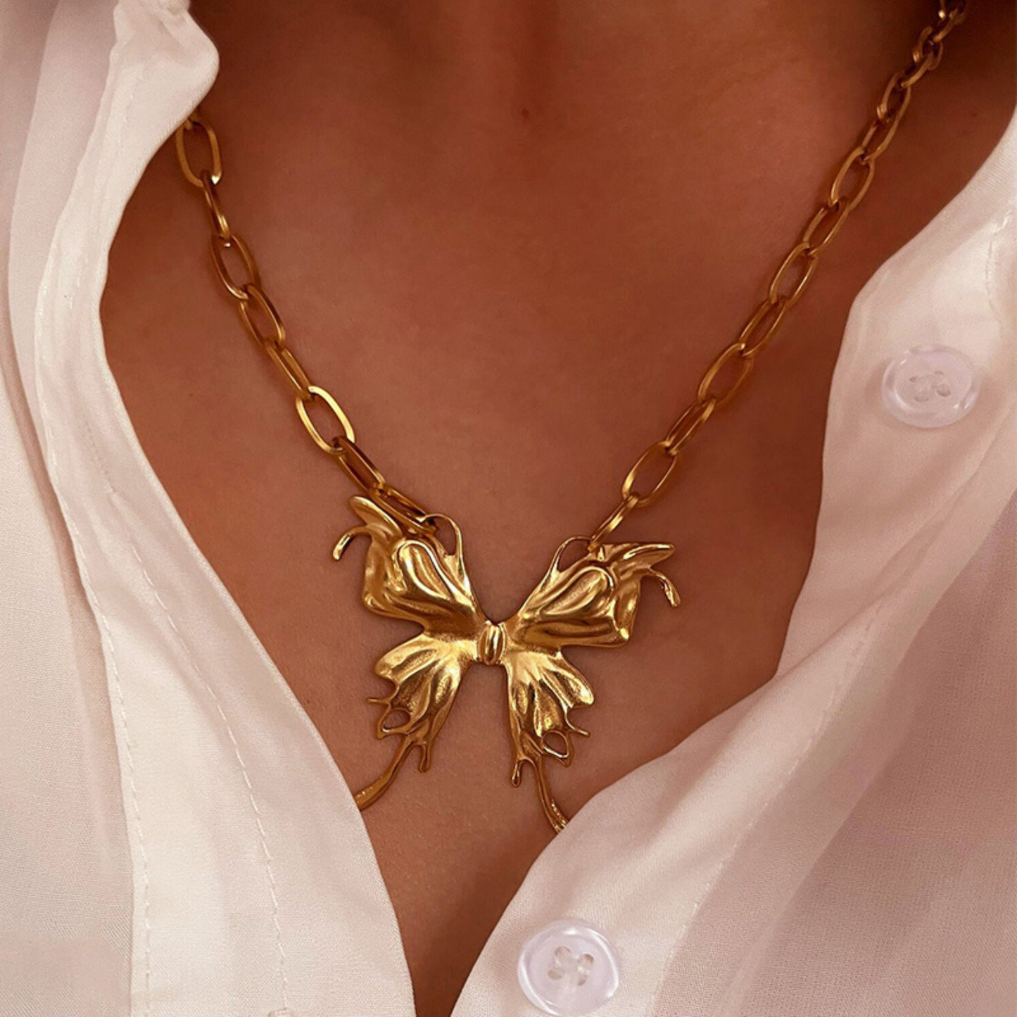Gold necklace with a butterfly design worn by a person wearing a white shirt.