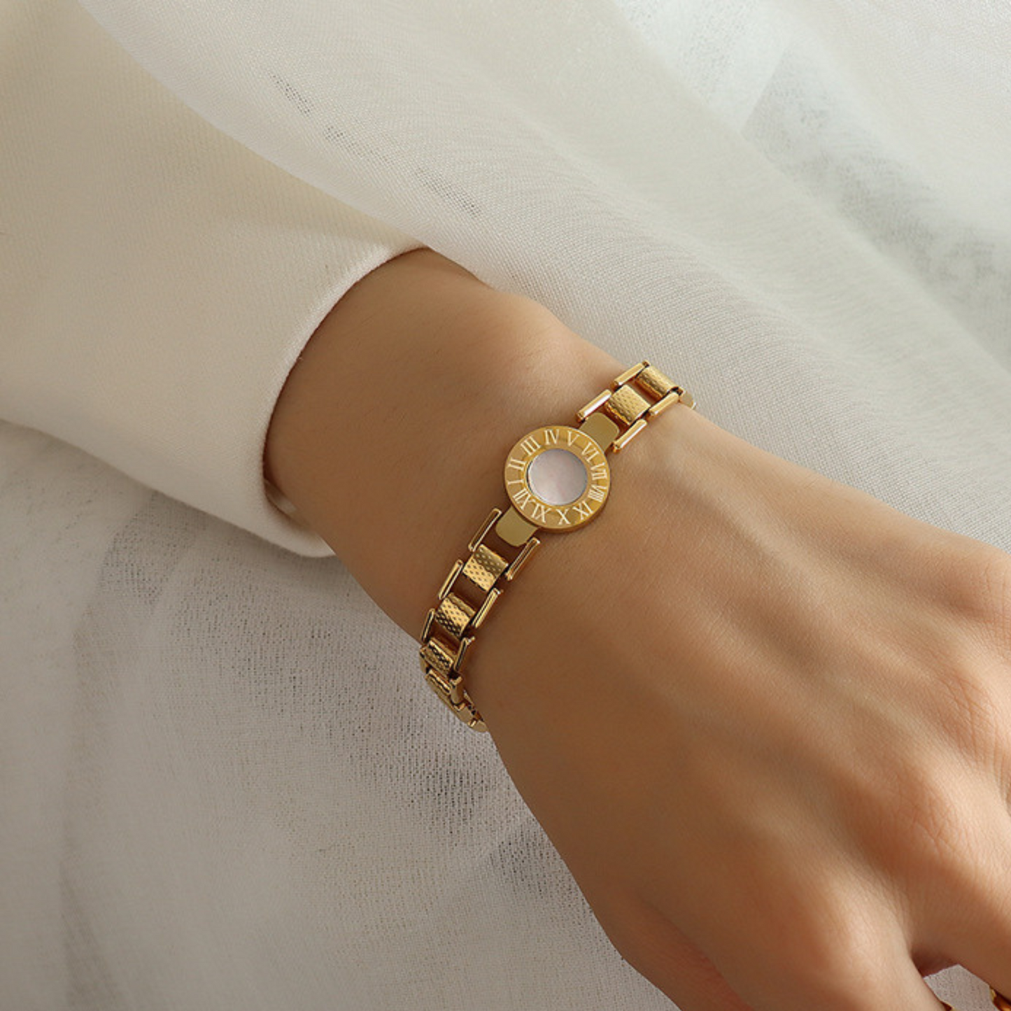 Gold bracelet on a wrist against a neutral background