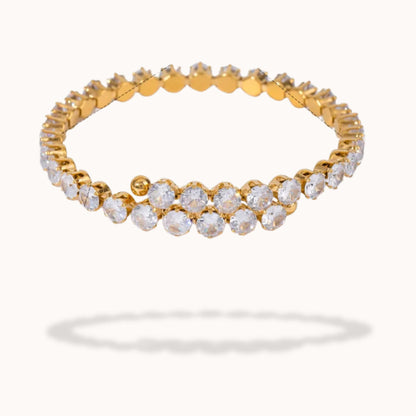A gold-plated eternity-style bracelet adorned with clear round-cut gemstones, shown against a plain off-white background with a soft shadow beneath.