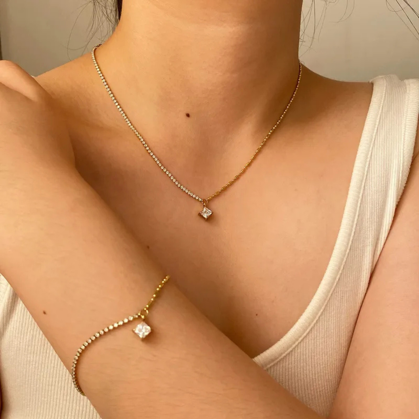 Close-up of a person wearing a delicate gold necklace and bracelet with a small diamond pendant.