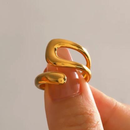 Gold ring with a unique design on a finger against a neutral background