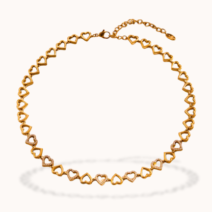 A gold heart-link chain necklace displayed on a clean, off-white background with a soft shadow underneath.