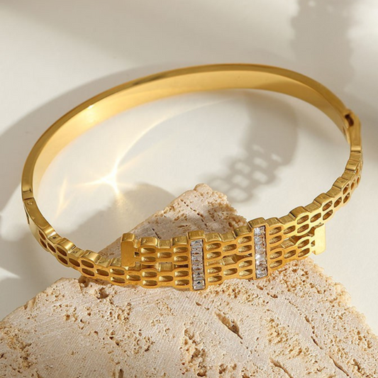 Gold bracelet with a textured design on a beige stone surface