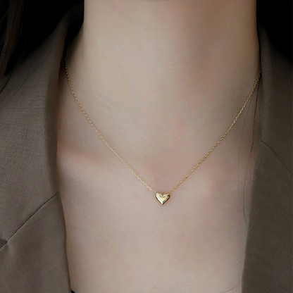 Gold heart necklace on a person's neck against a neutral background