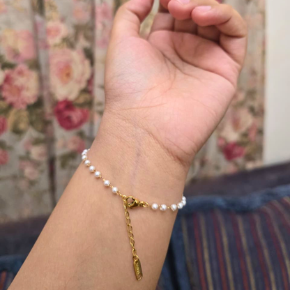Hand wearing a pearl bracelet with a gold chain and tag against a floral background
