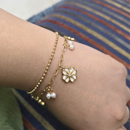 Gold bracelet with a flower charm and pearl beads on a wrist against a striped background