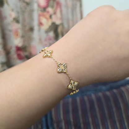 Gold bracelet with floral designs on a wrist against a floral curtain background