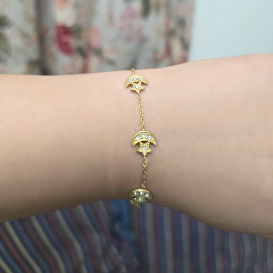 Gold bracelet with moon and star designs on a wrist against a blurred background