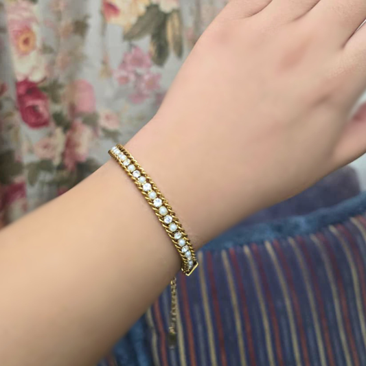 Gold bracelet with clear stones on a wrist against a floral and striped fabric background