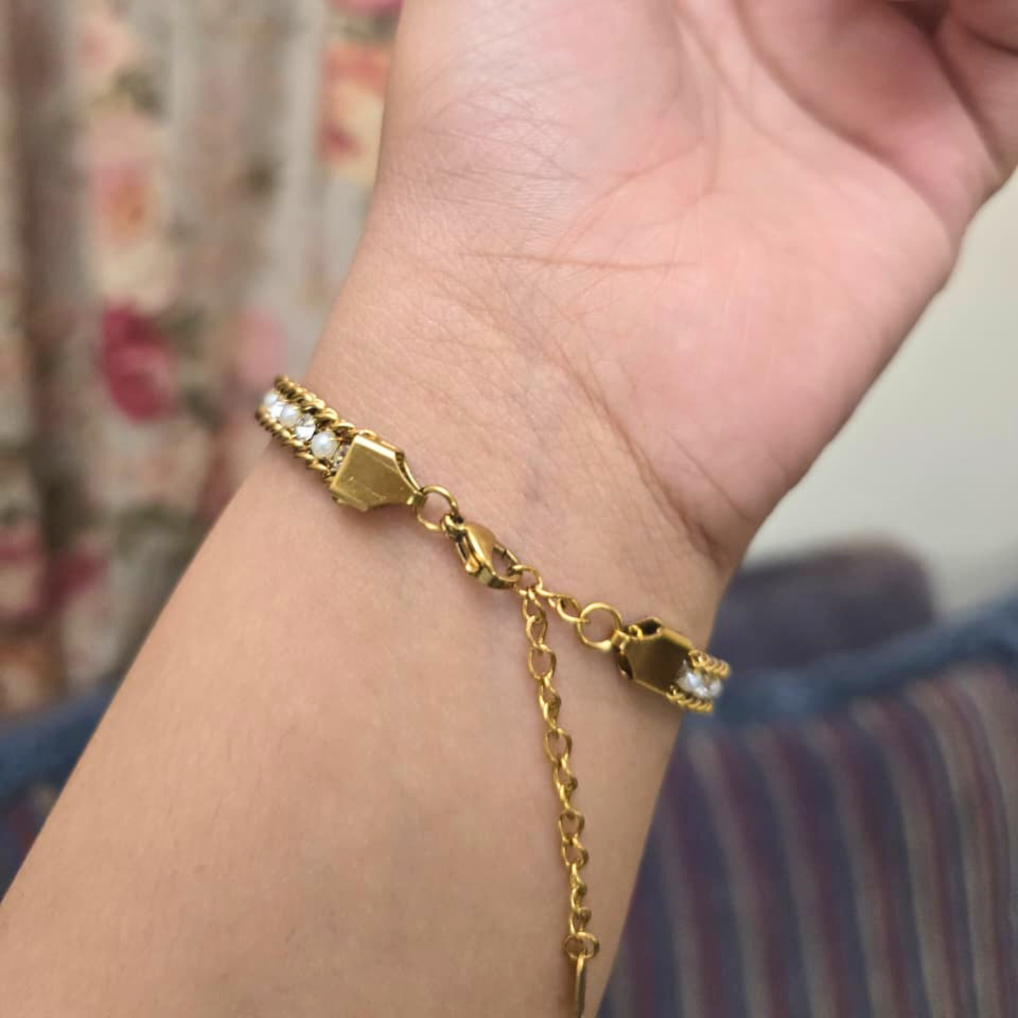 Gold bracelet on a wrist with a floral background