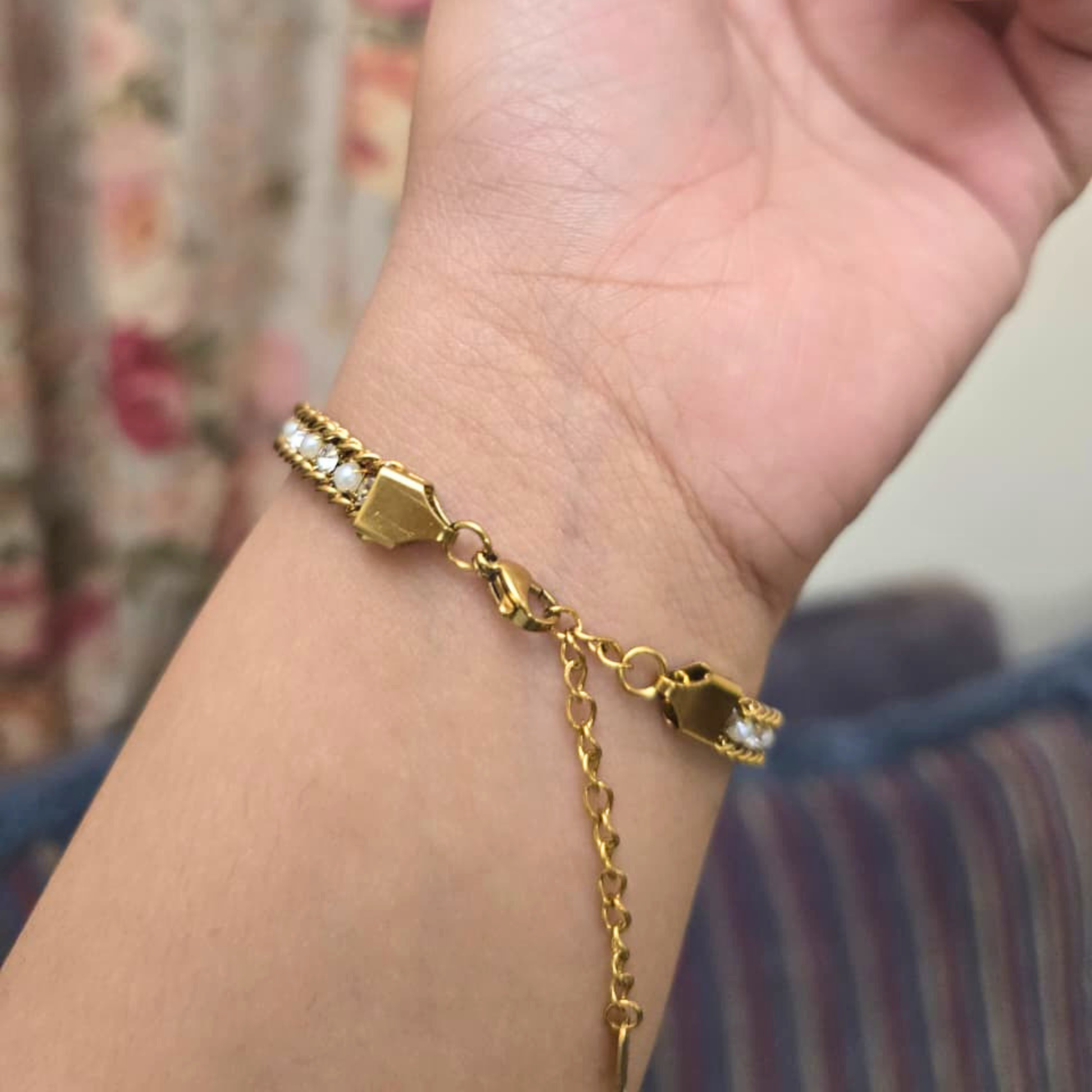 Gold bracelet on a wrist with a floral background