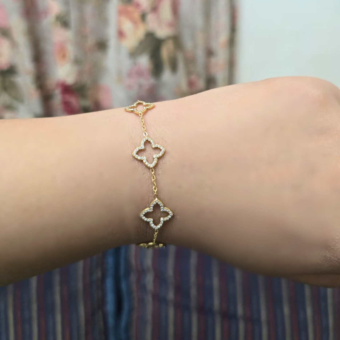 Gold bracelet with clover-shaped charms on a wrist against a floral background
