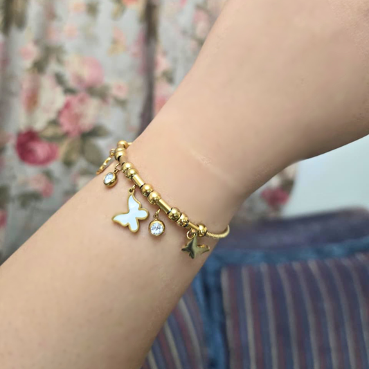 Gold bracelet with butterfly charm on a wrist against a floral background