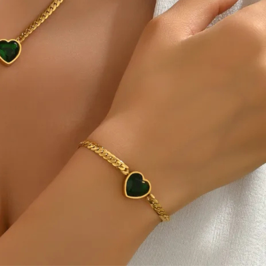 Gold bracelet with green heart charm on a wrist against a neutral background