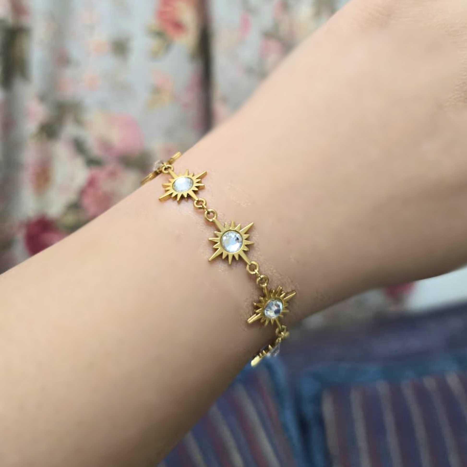 Gold bracelet with sun designs on a wrist against a floral background
