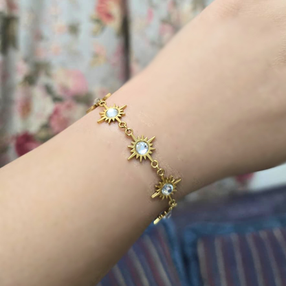 Gold bracelet with sun designs on a wrist against a floral background