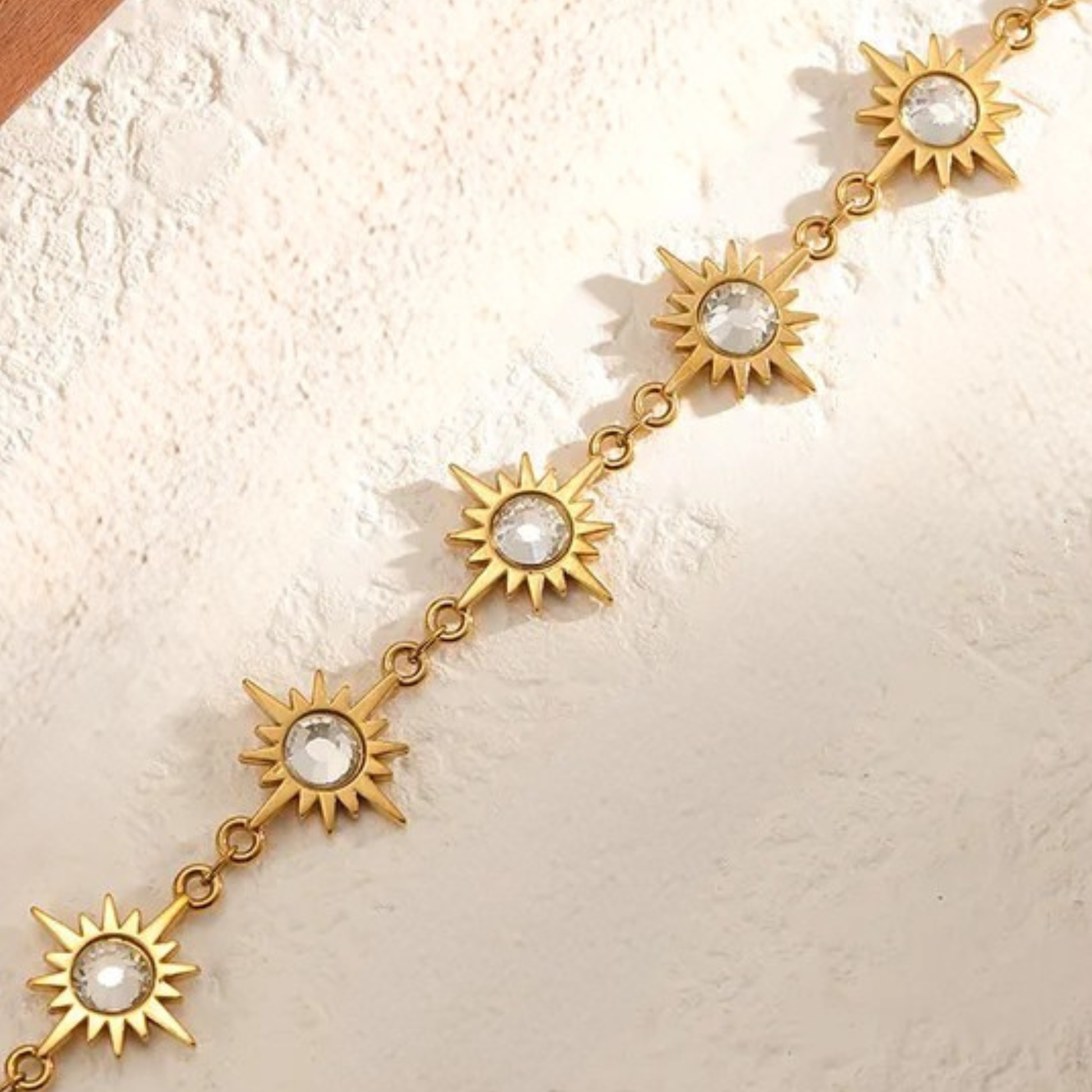 Gold necklace with sun-shaped pendants on a textured beige surface