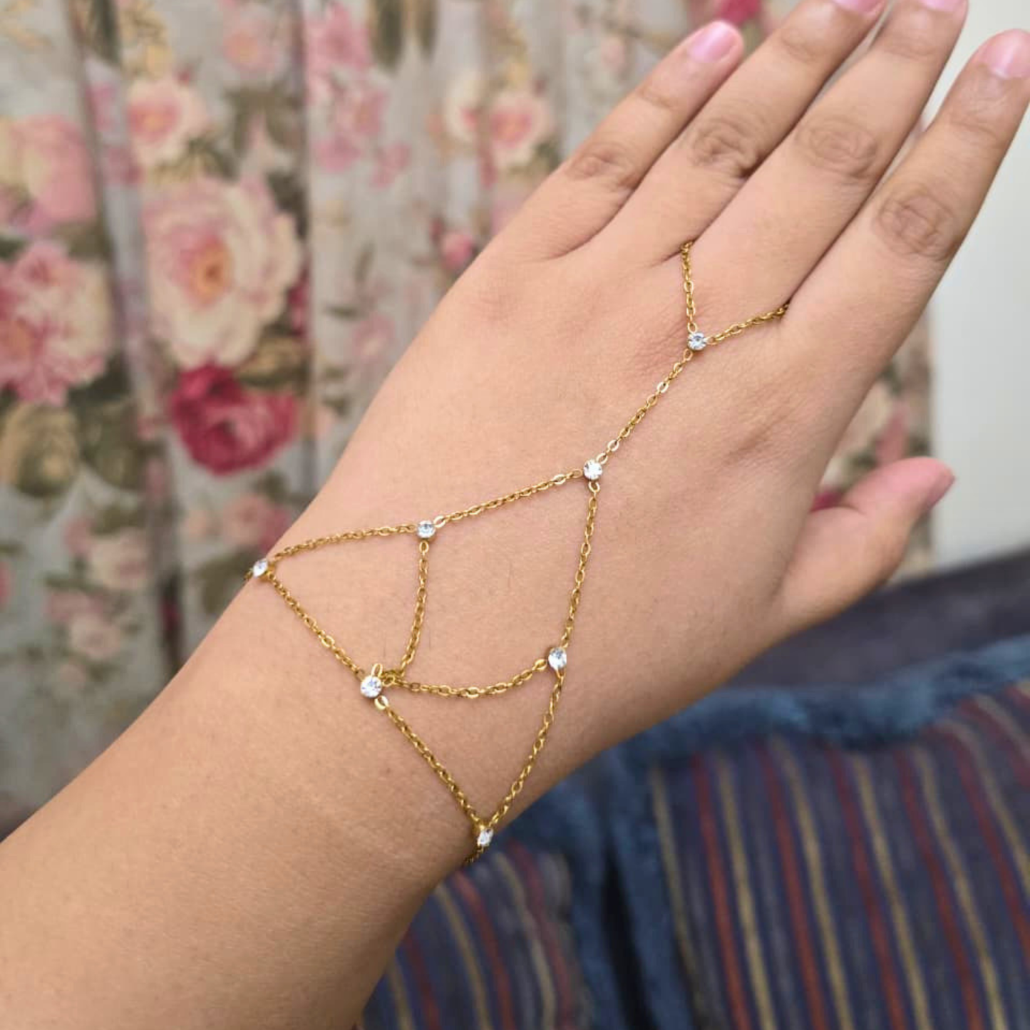 Gold chain bracelet on a hand with a floral background