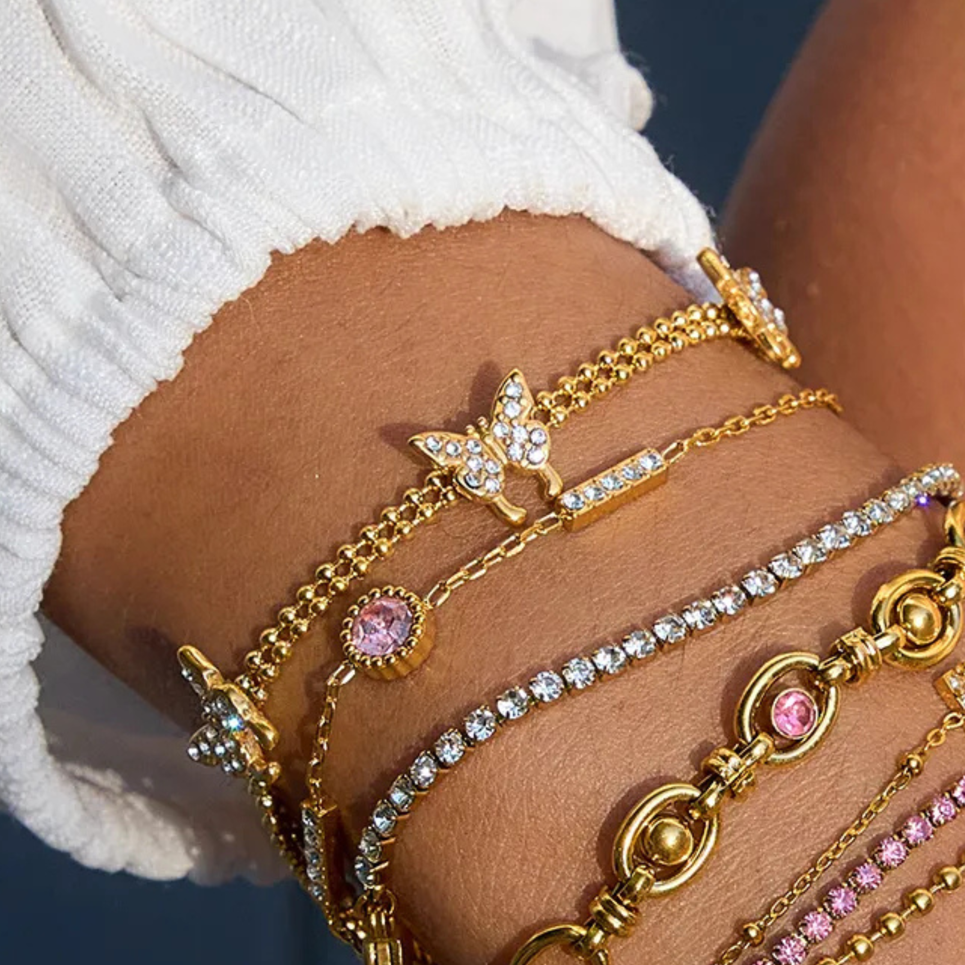 Gold and pink beaded bracelets on a wrist with a white sleeve.