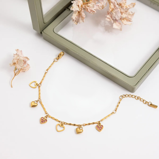 Gold bracelet with heart charms on a white surface with a green jewelry box in the background.
