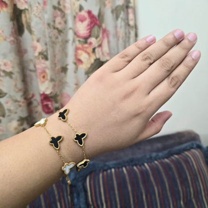 Hand wearing a gold bracelet with butterfly charms against a floral curtain background