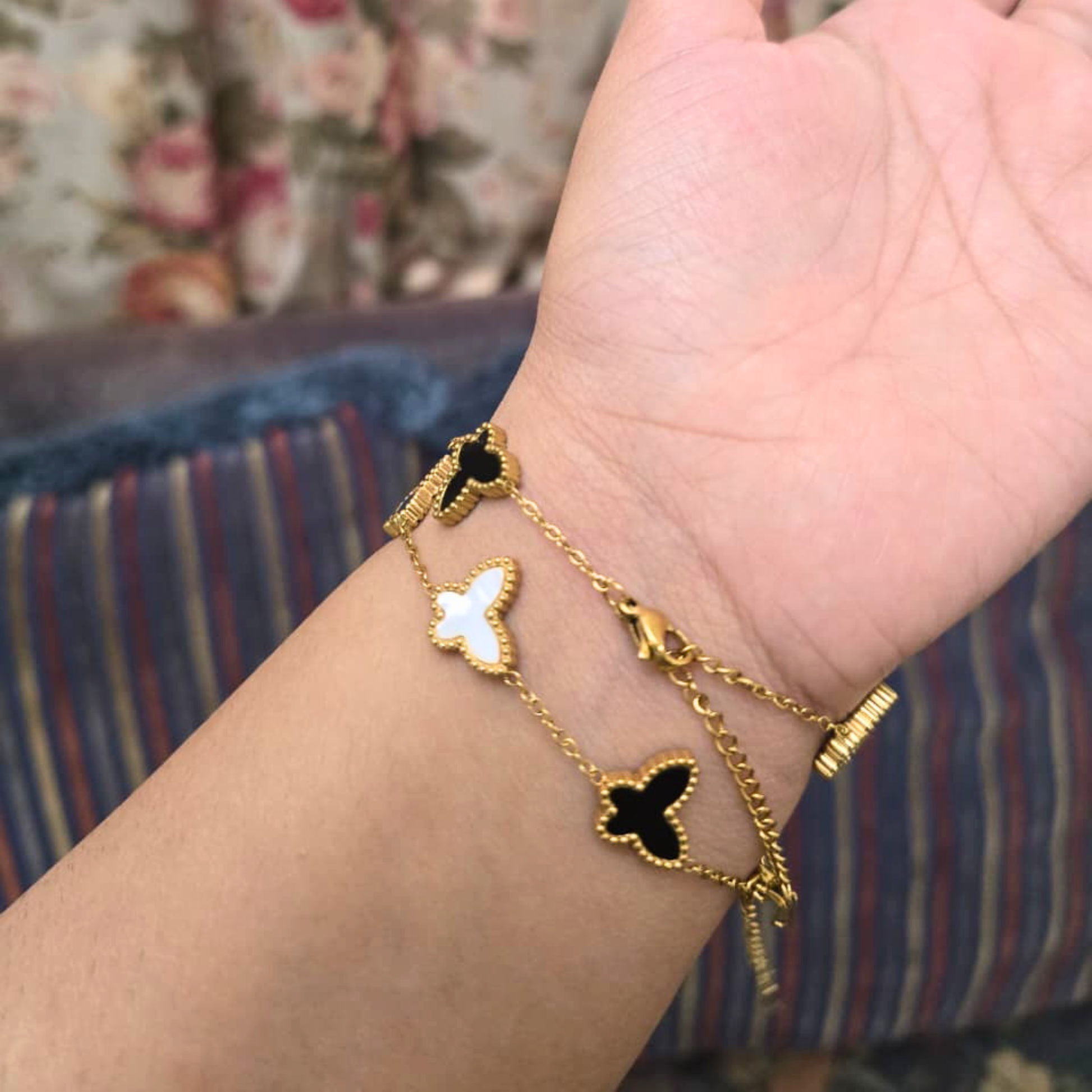Gold bracelet with black heart charms on a wrist against a floral background