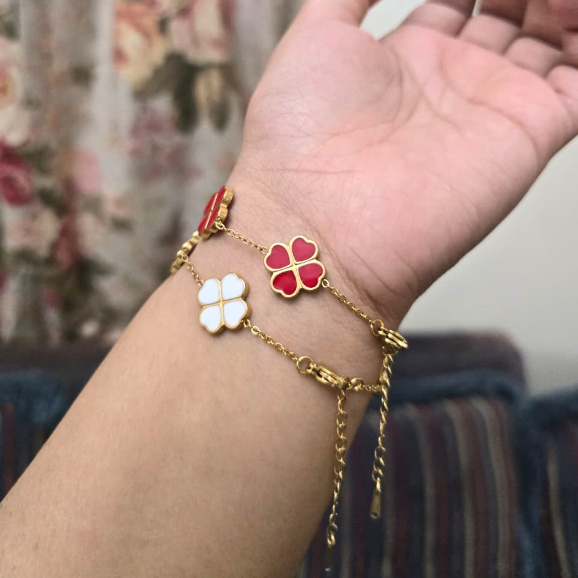 Gold bracelet with red and white flower charms on a wrist against a blurred background