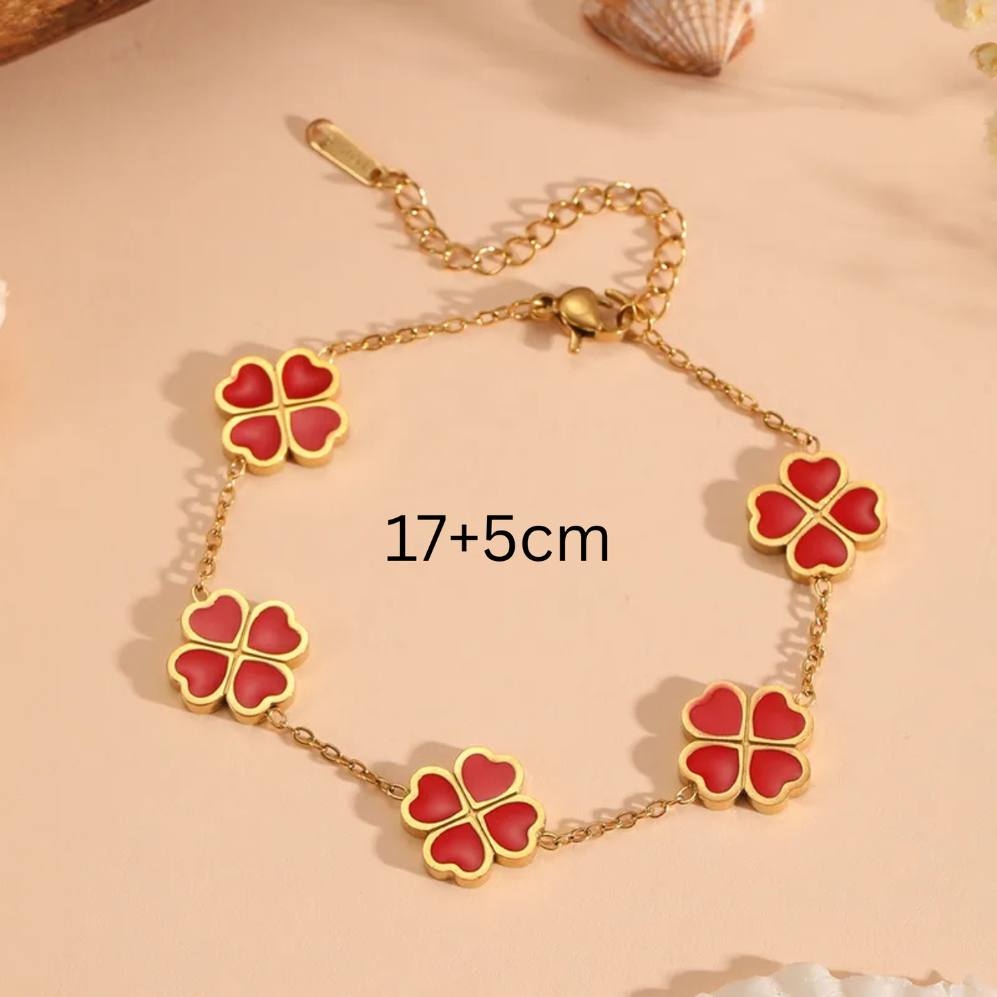 Gold bracelet with red clover-shaped charms on a beige background