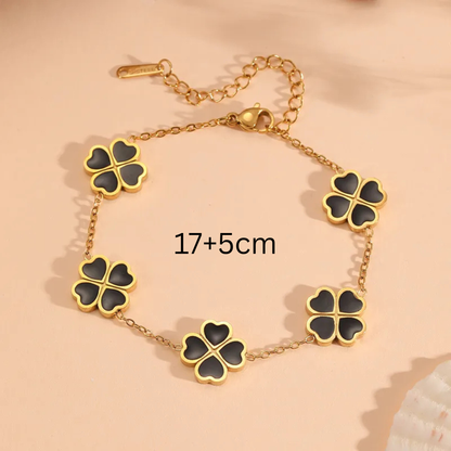Gold bracelet with black clover-shaped charms on a beige background