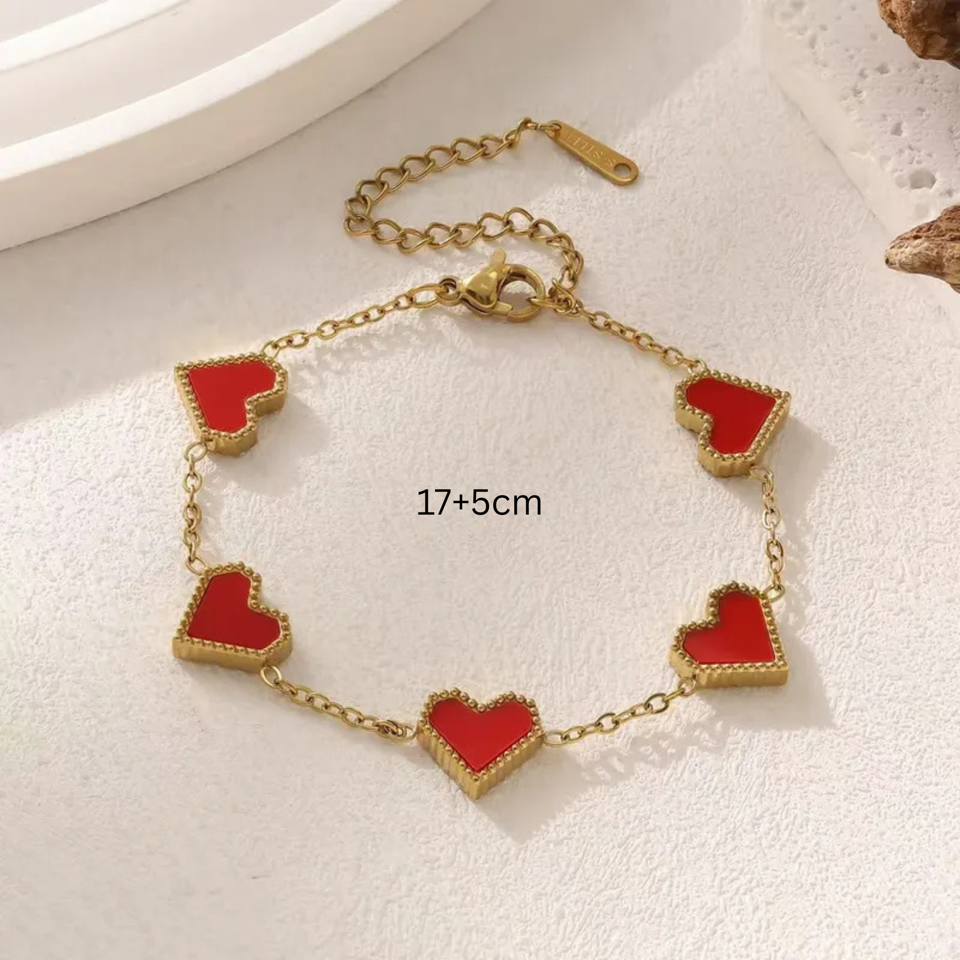 Gold bracelet with red heart charms on a light background