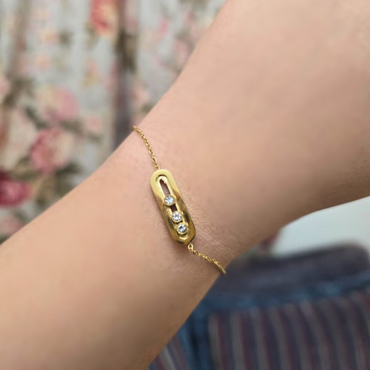 Gold bracelet with a decorative clasp on a wrist against a blurred floral background