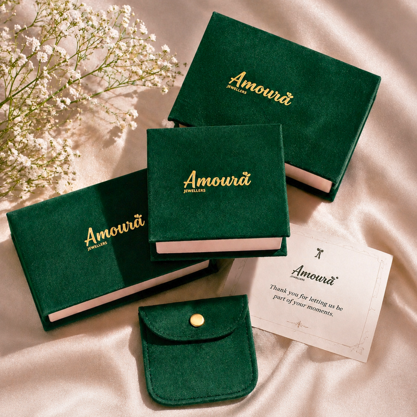 Green jewelry boxes with 'Amoura' branding on a soft fabric background.