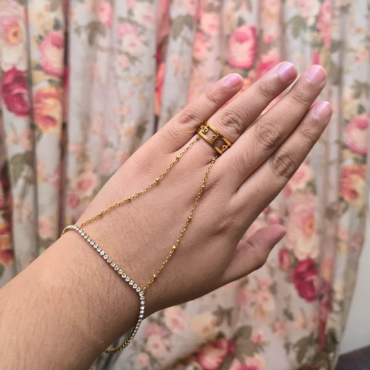 Hand wearing a gold ring and bracelet with a floral curtain background