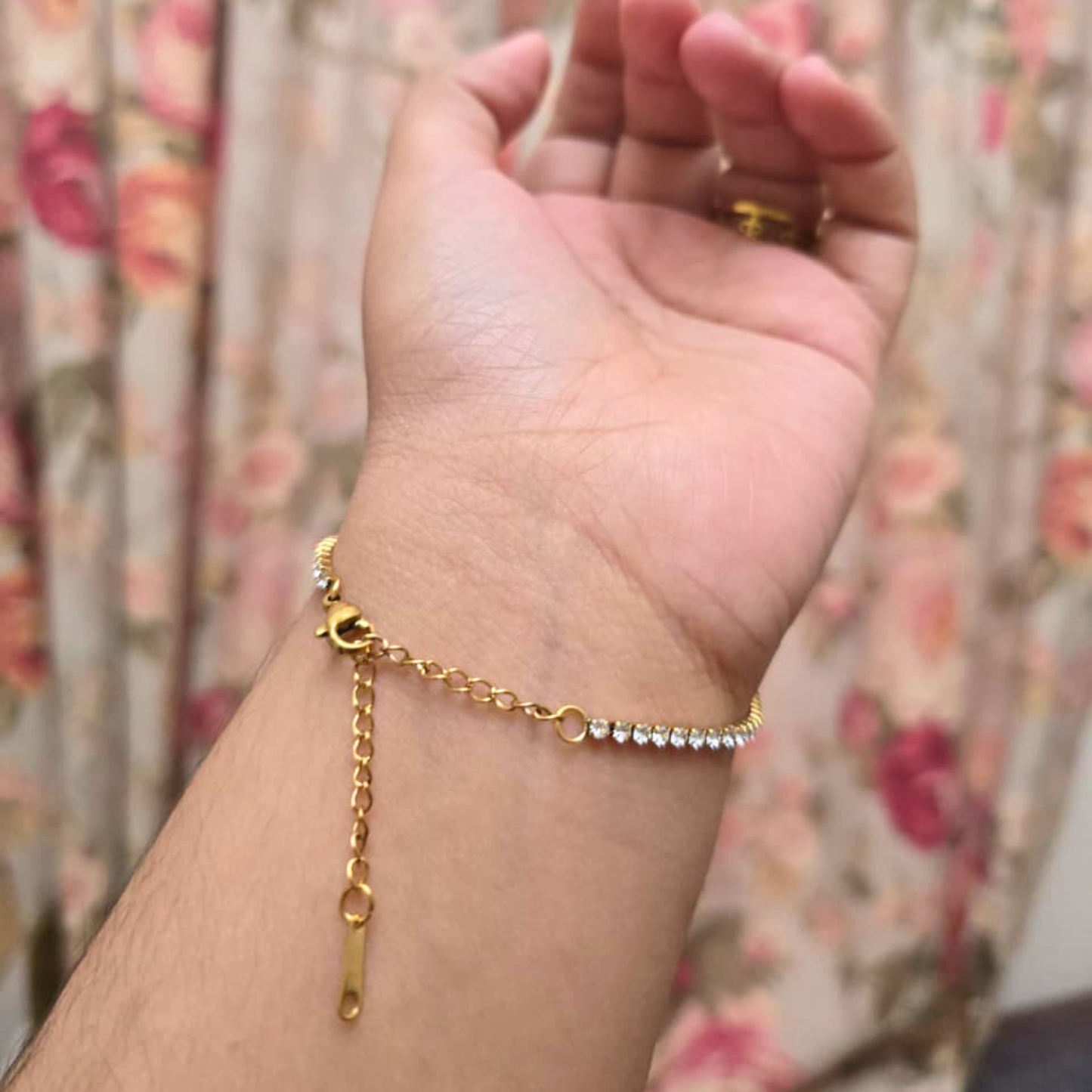 Gold bracelet on a wrist with a floral background