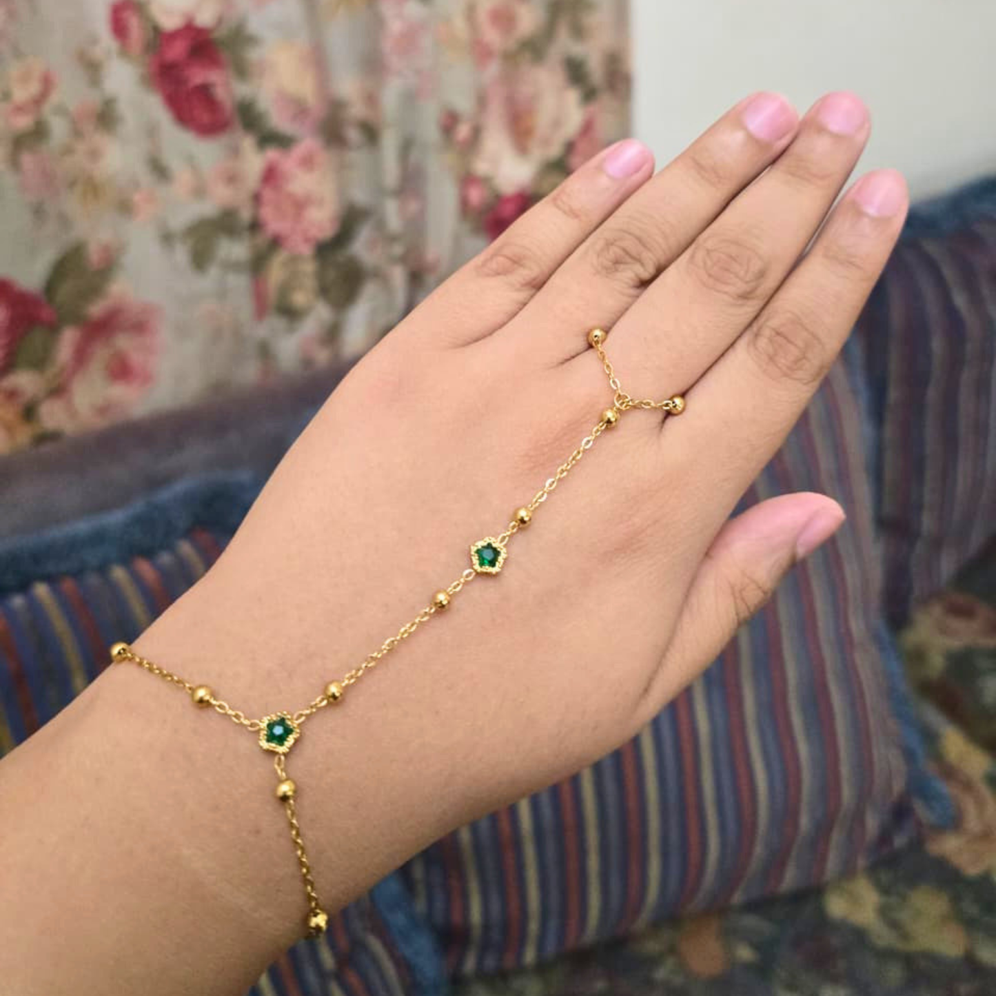 Gold bracelet with green gemstones on a hand against a floral background