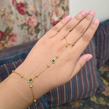Gold bracelet with green gemstones on a hand against a floral background