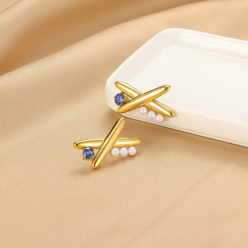 Gold earrings with blue gemstones and pearls on a beige surface