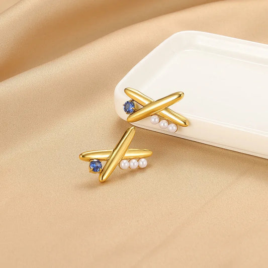 Gold earrings with blue gemstones and pearls on a beige surface