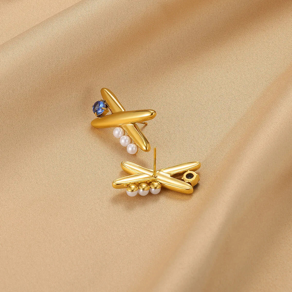 Gold earrings with pearls and gemstones on a beige fabric background