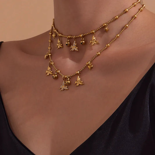 Gold necklace with floral pendants on a person wearing a black top against a beige background