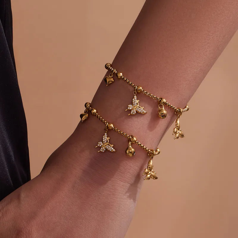 Gold bracelet with butterfly charms on a wrist against a beige background
