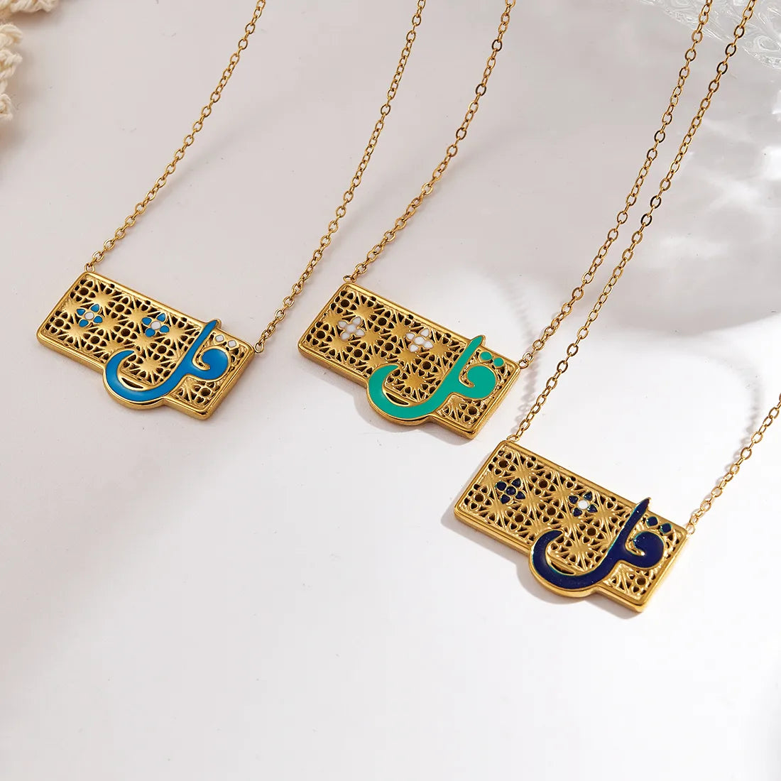 Three gold necklaces with Arabic calligraphy pendants on a white background