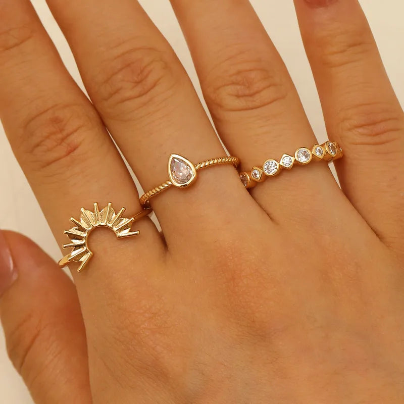Hand wearing three gold rings with different designs on a neutral background