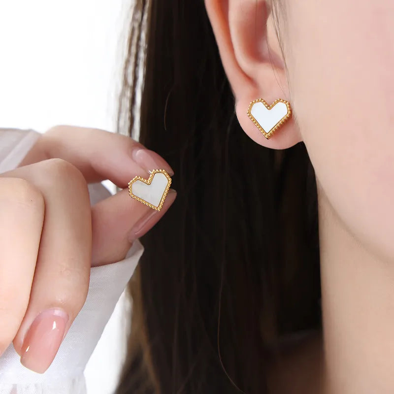 Heart-shaped earrings being worn and held up to the ear.