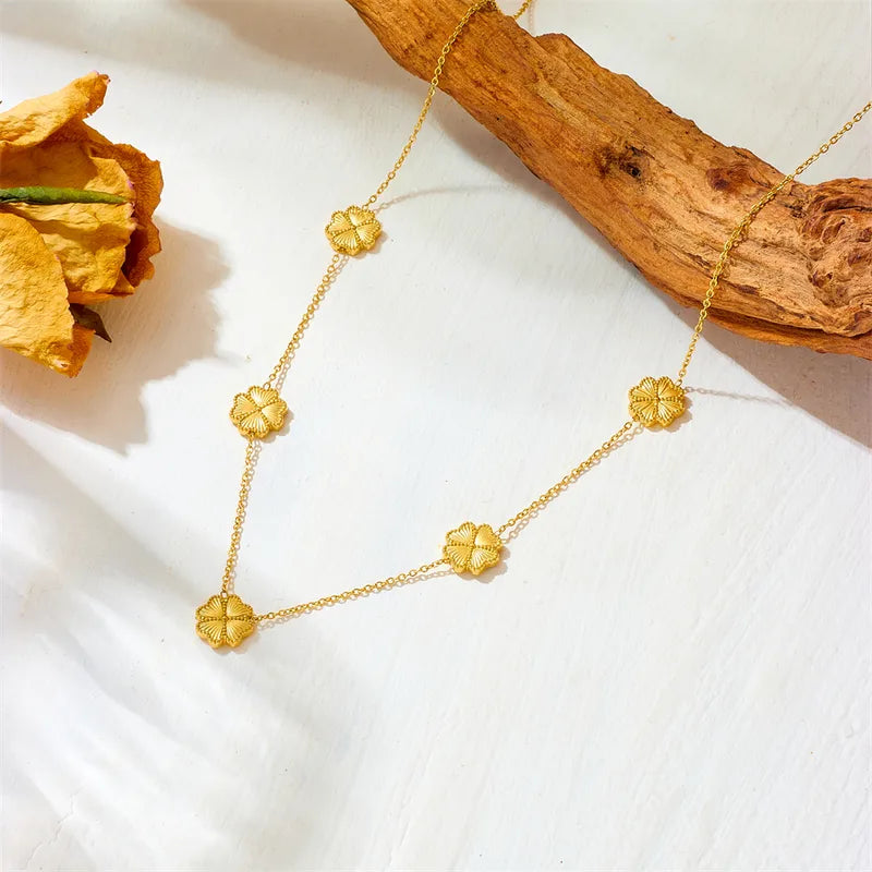 Gold necklace with floral pendants on a white surface with a wooden branch and dried flower.