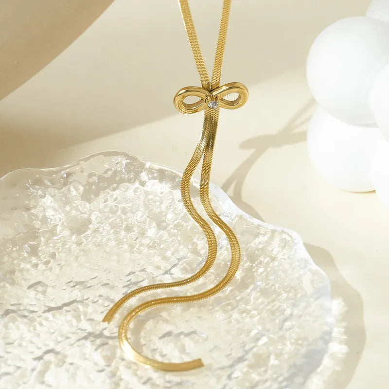 Gold necklace with a bow-shaped pendant on a textured white surface