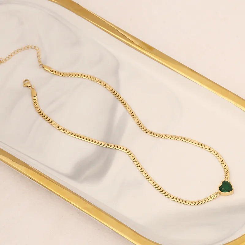 Gold chain necklace with a green heart pendant on a white and gold surface