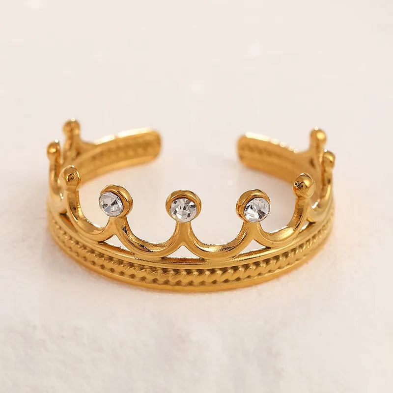 Gold crown-shaped ring with embedded crystals on a light beige background